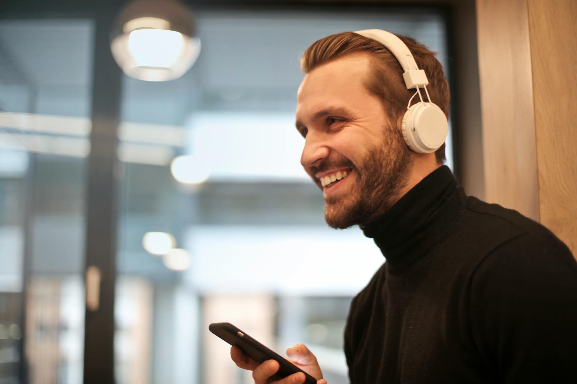 Un hombre sonriente con unos auriculares blancos y el teléfono en la mano | Fuente: Pexels