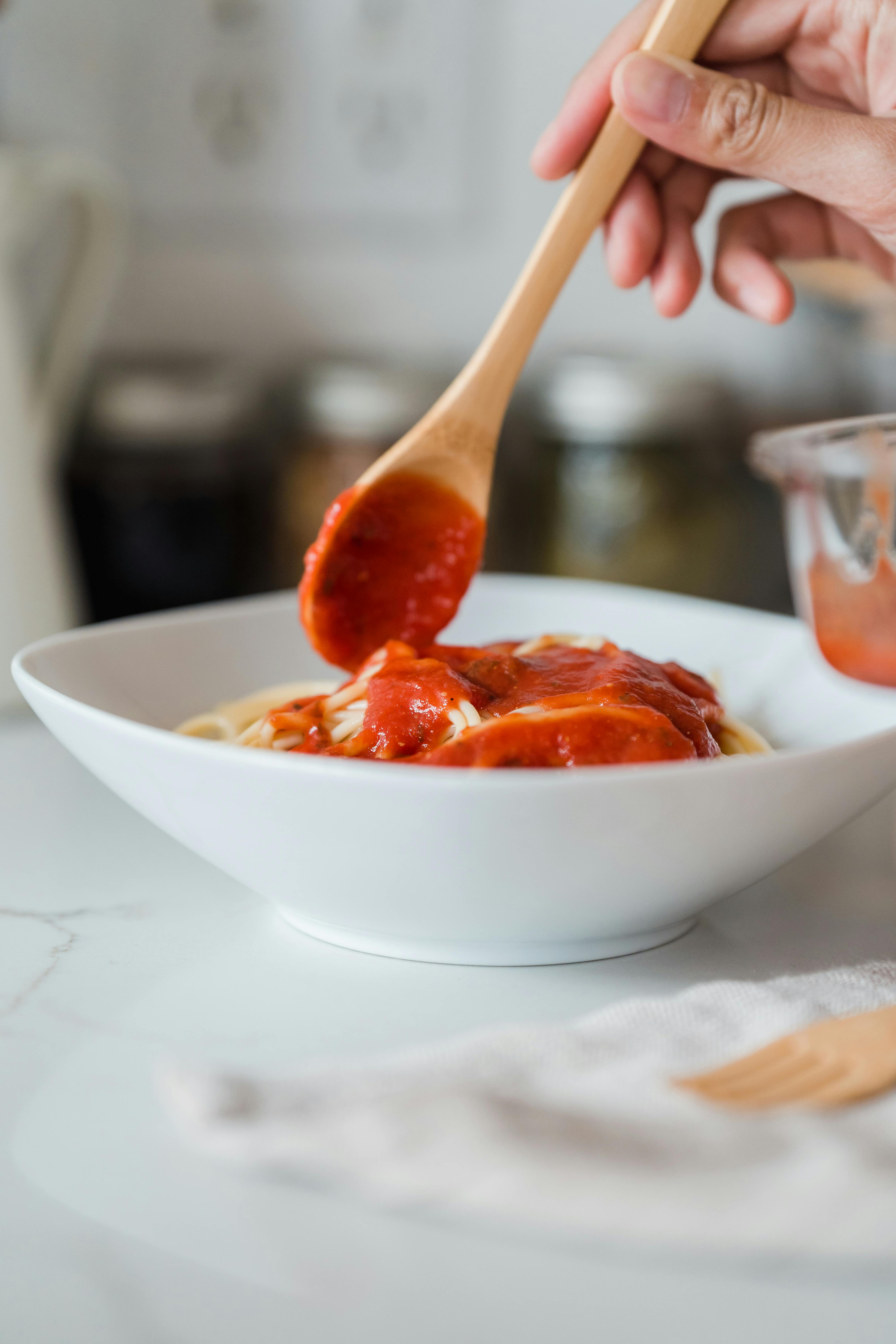 Una persona añadiendo salsa a la pasta | Fuente: Pexels