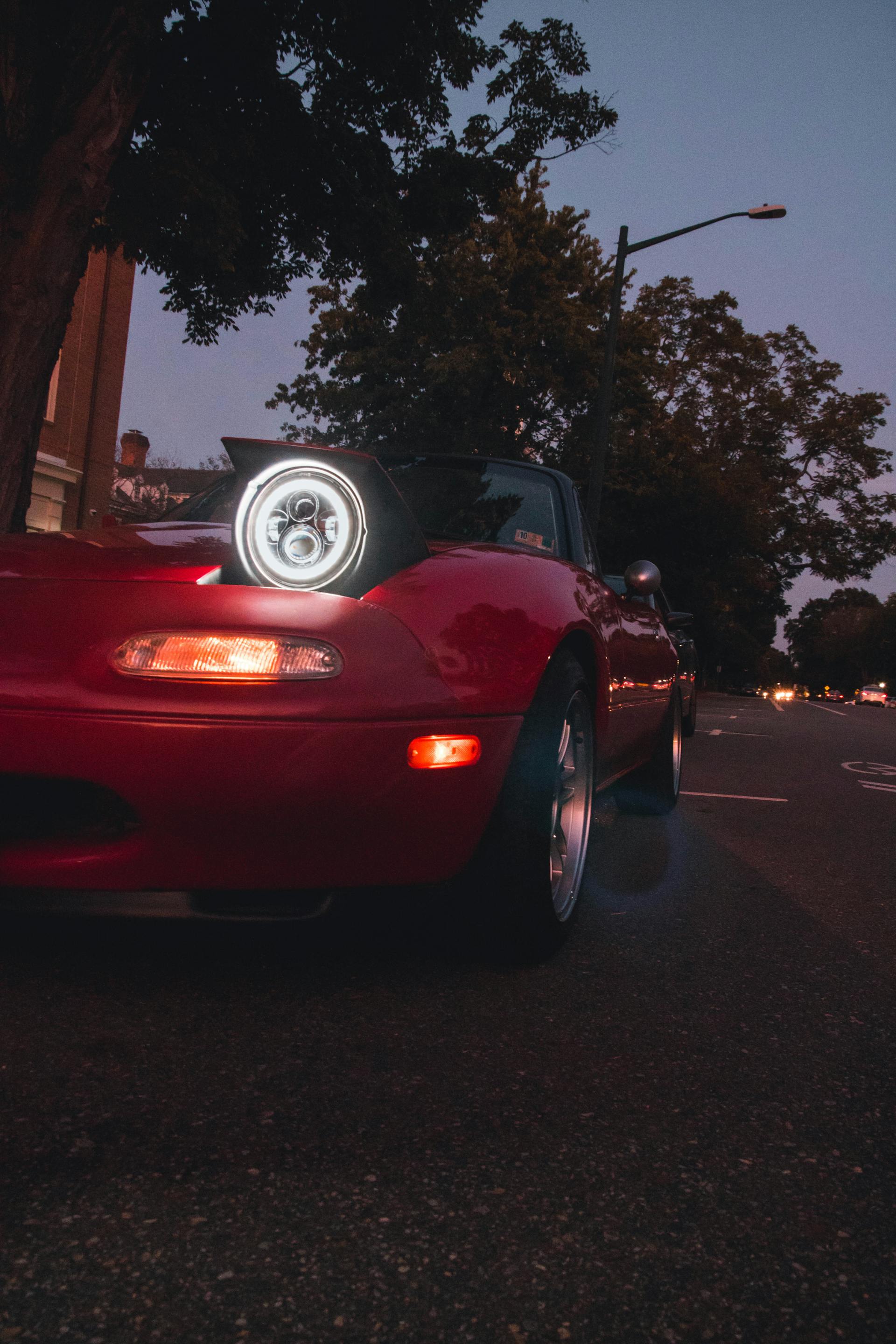 Un automóvil rojo con los faros encendidos por la noche | Fuente: Pexels