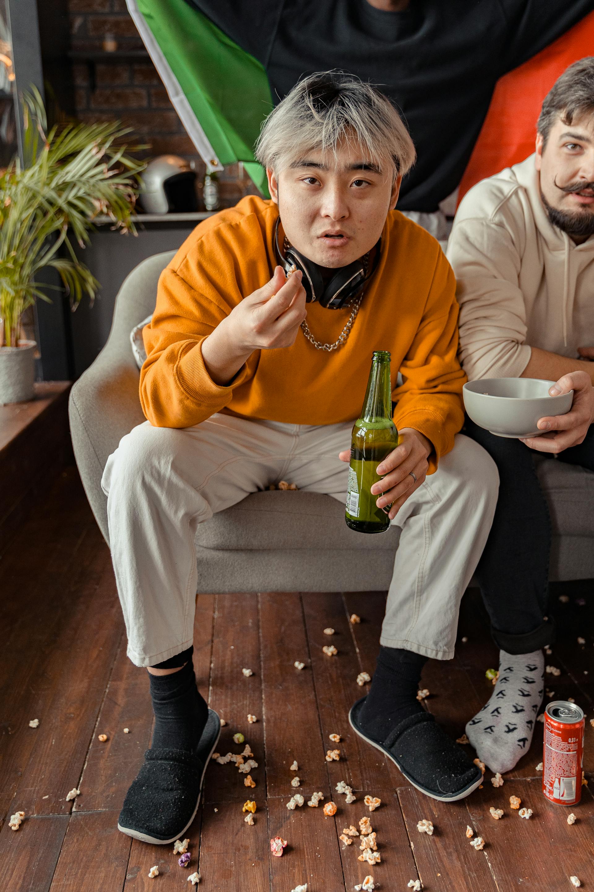 Dos hombres sentados en el sofá tomando cerveza y palomitas | Fuente: Pexels