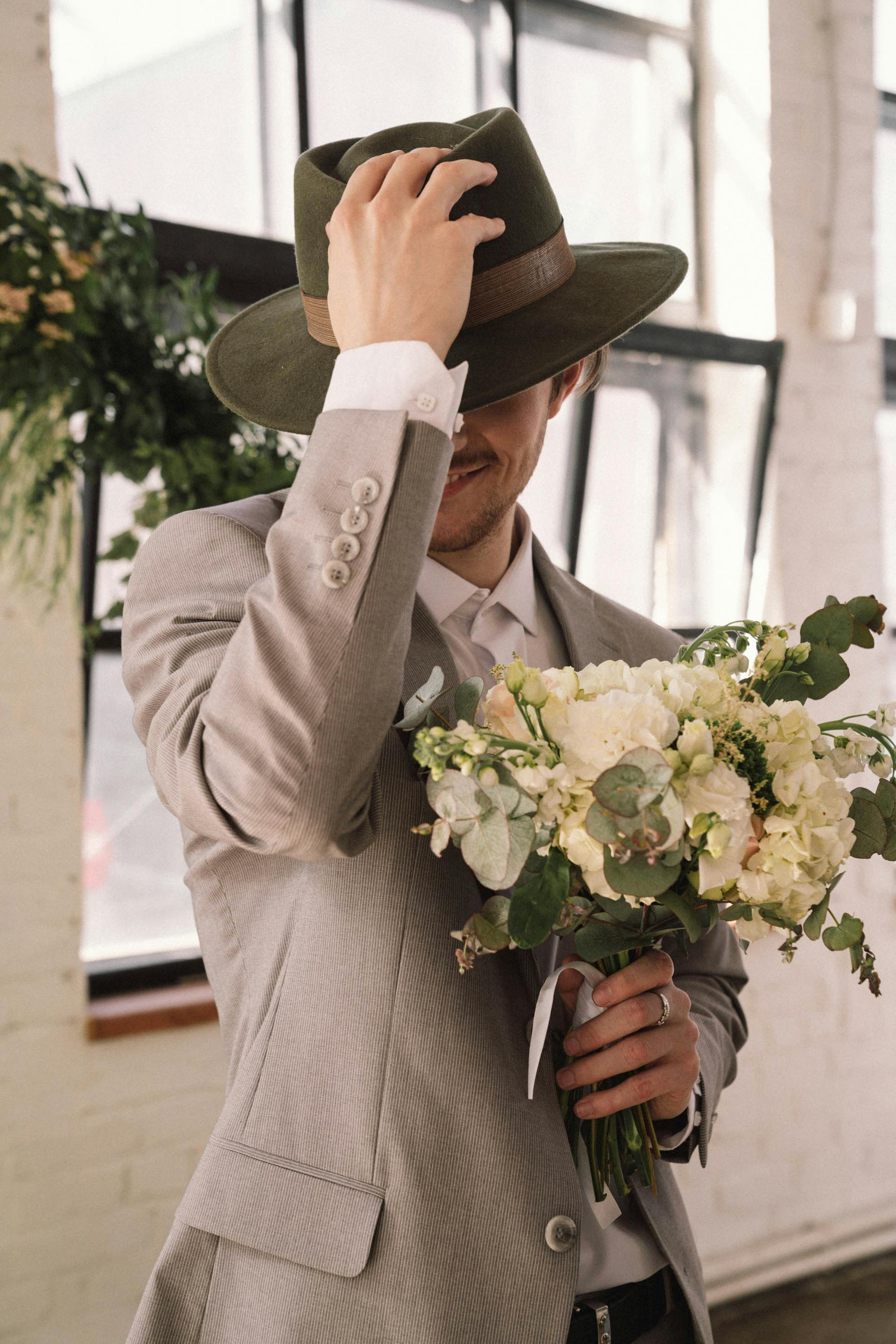 Hombre con traje gris y sombrero sosteniendo flores | Fuente: Pexels