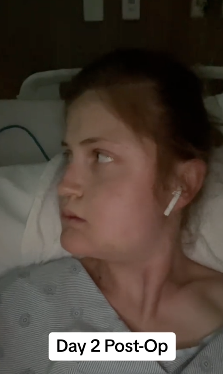 Con una bata de hospital y un AirPod, Virginia Elder mira de reojo durante su segundo día de curación | Fuente: TikTok/virginiaeelder