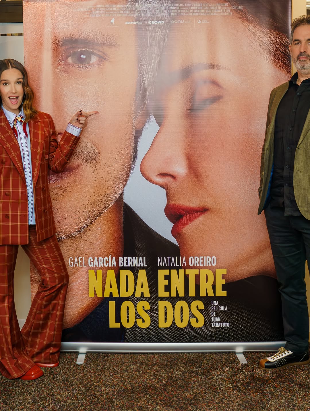 Natalia Oreiro y Juan Taratuto posan junto al afiche de “Nada entre los dos” durante la presentación de la película. La actriz señala el póster mientras luce su conjunto sastrero de cuadros rojizos y el director aparece con saco verde oliva y camisa oscura. | Fuente: Instagram/nataliaoreirosoy