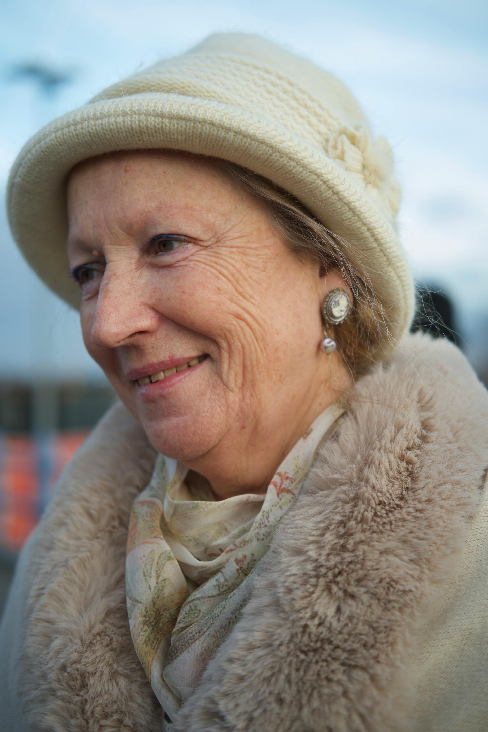Mujer mayor sonriente con abrigo de piel blanco y gorro tejido | Fuente: Pexels