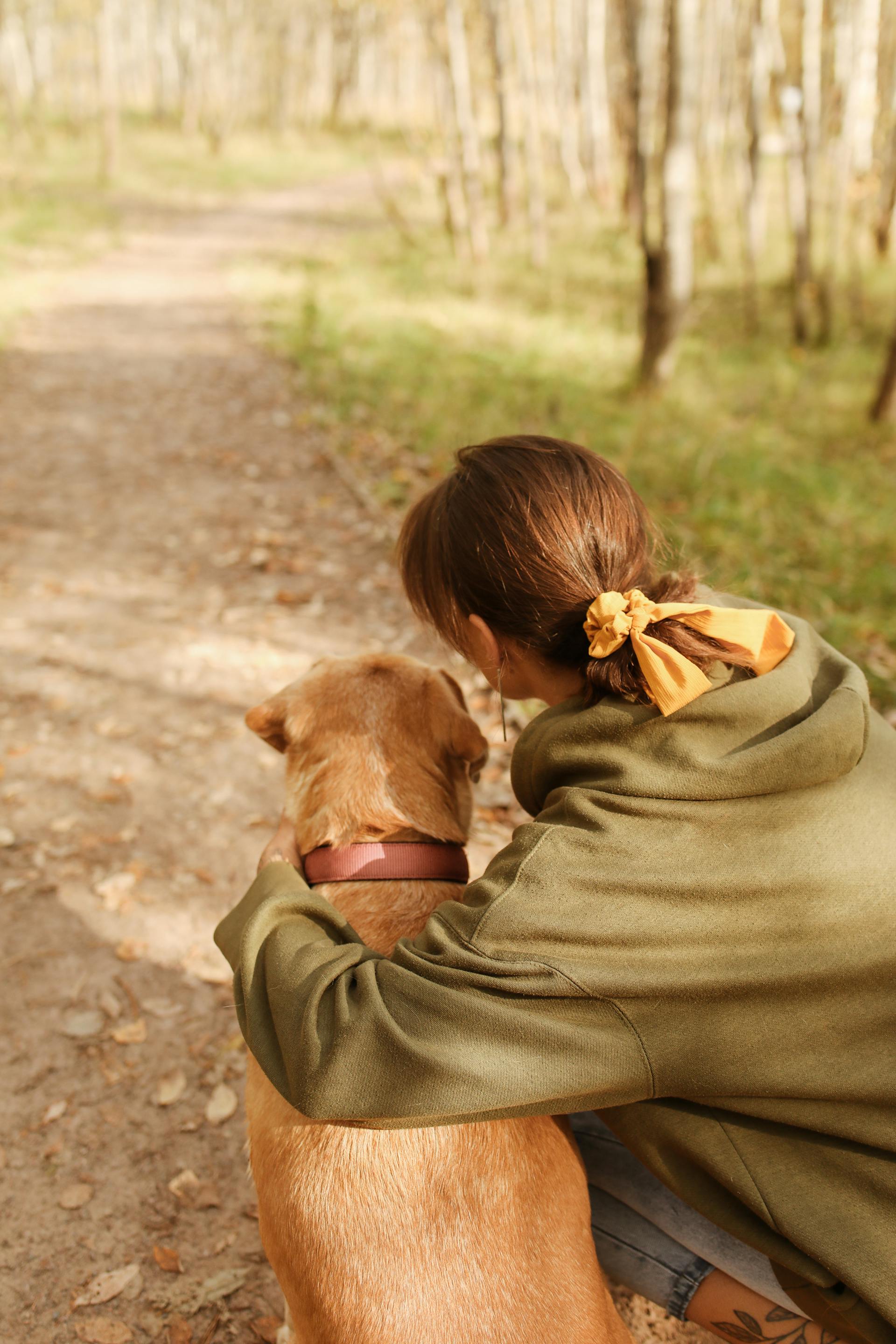 Vista trasera de una mujer arrodillada junto a su perro | Fuente: Pexels