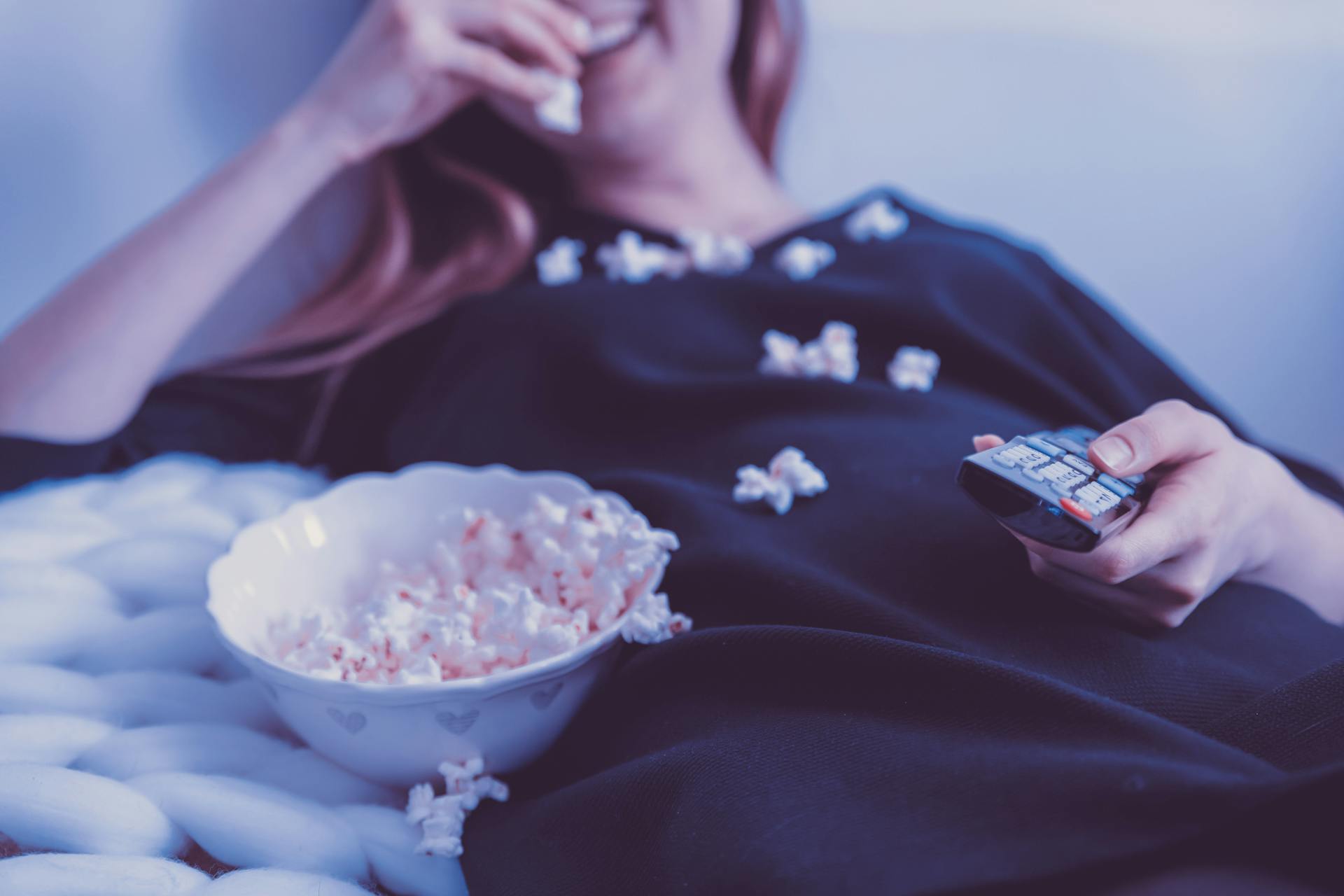 Una mujer comiendo palomitas mientras sujeta el mando de la tele | Fuente: Pexels