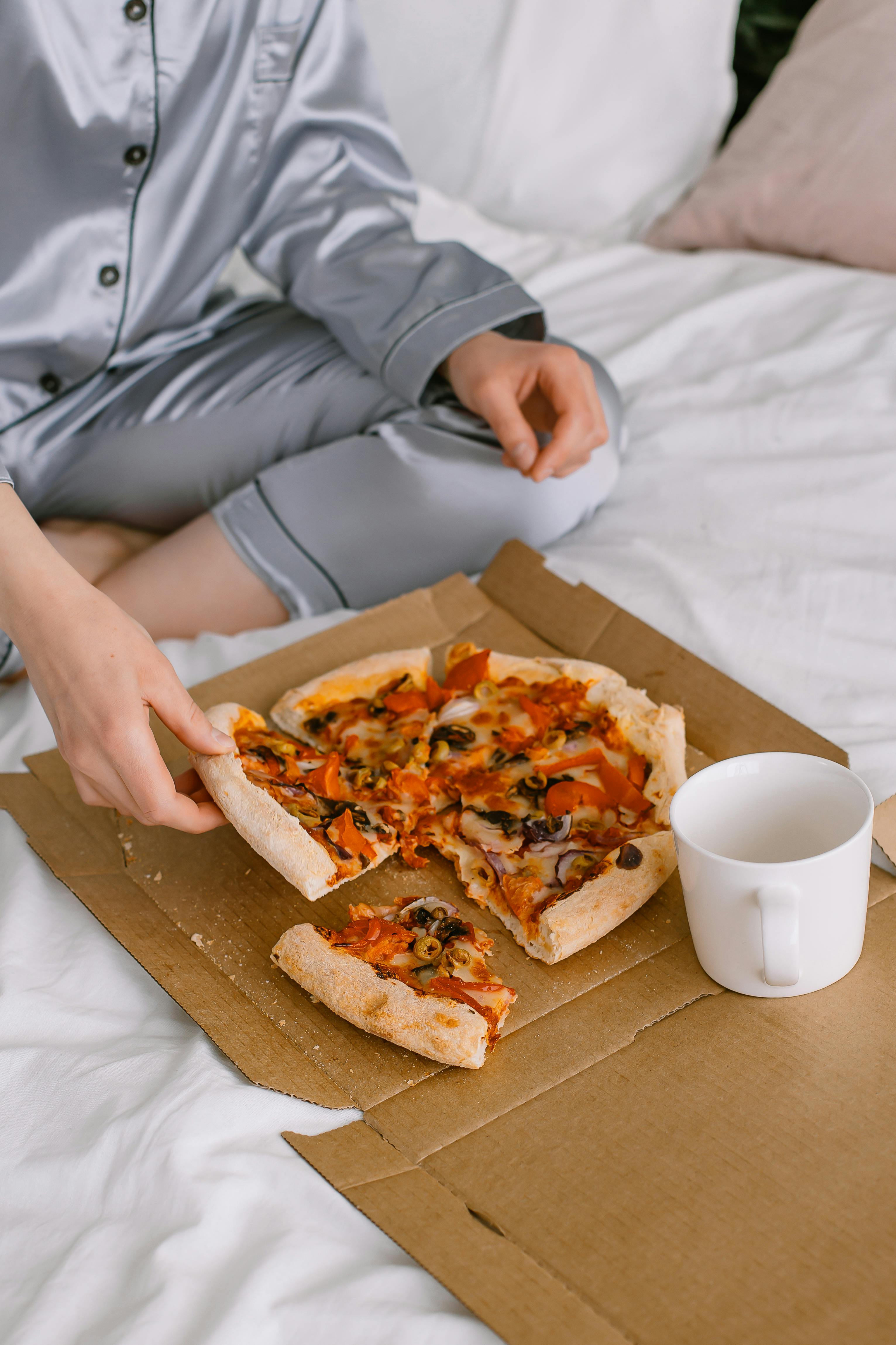 Una persona sentada en una cama con una caja de pizza | Fuente: Pexels