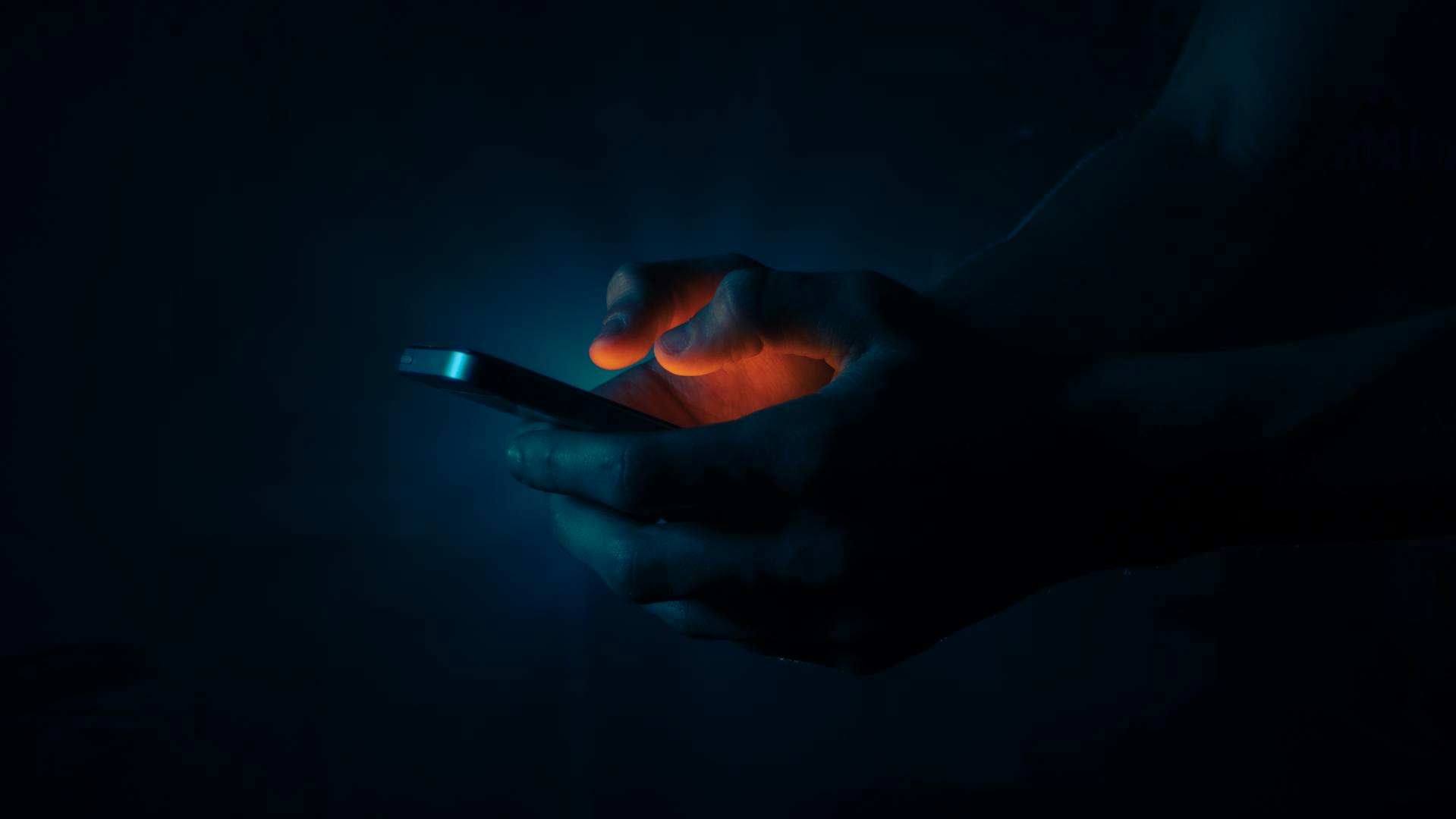 Un hombre sujetando un teléfono en la oscuridad | Fuente: Pexels
