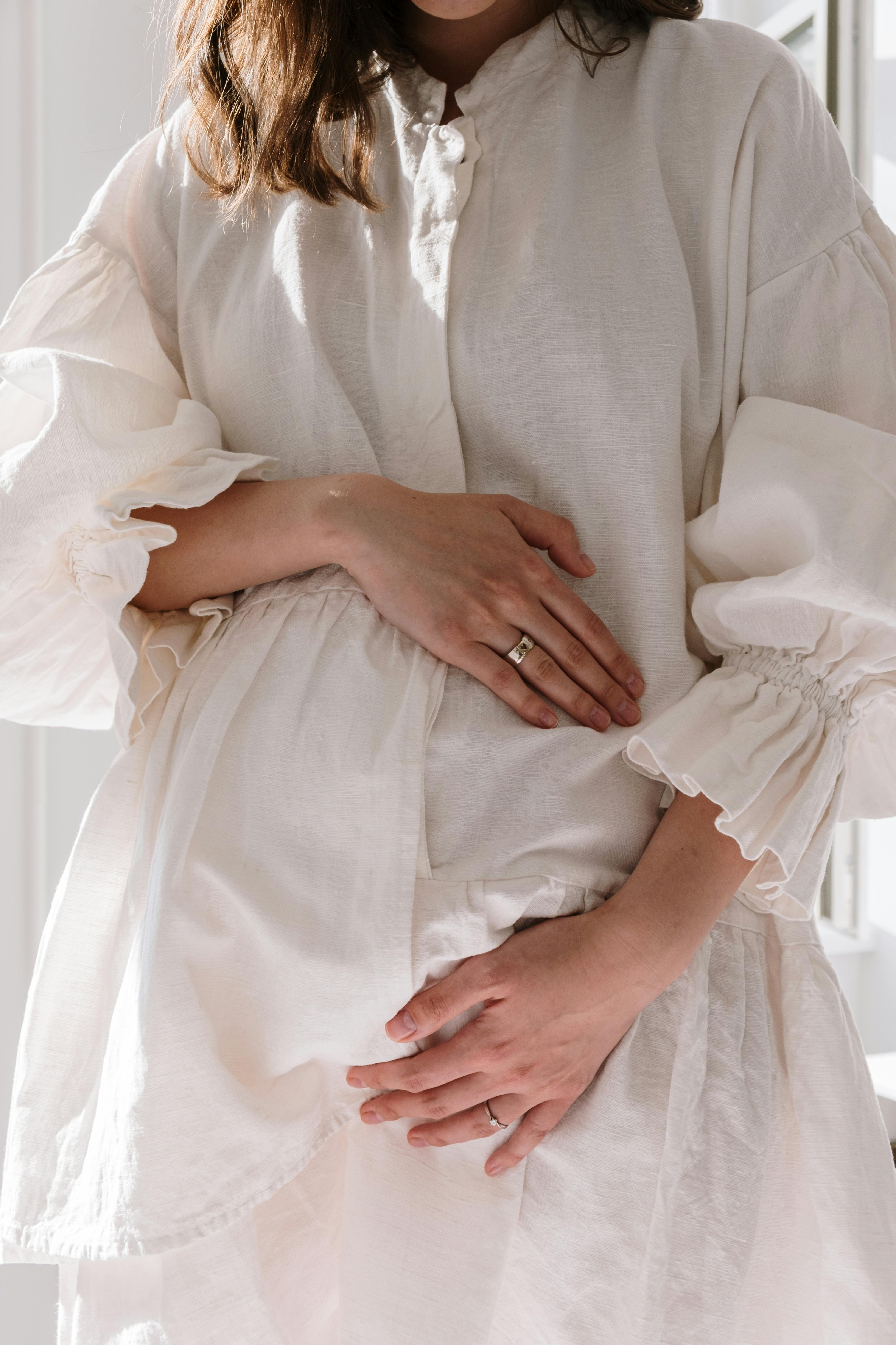 Una mujer con un vestido blanco sujetándose el vientre | Fuente: Pexels
