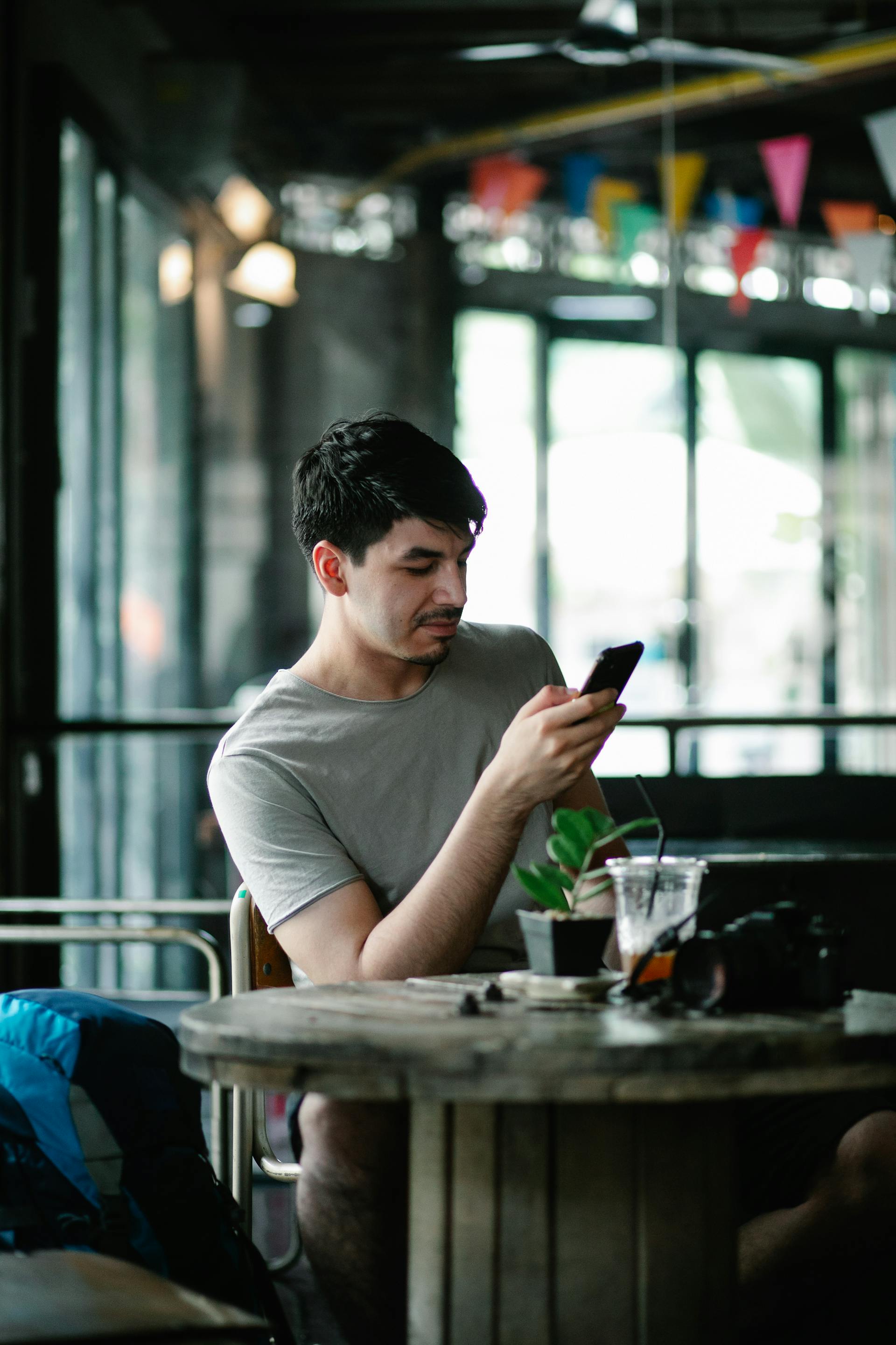 Un hombre moreno con camisa gris sentado en una mesa de una cafetería mirando su teléfono | Fuente: Pexels