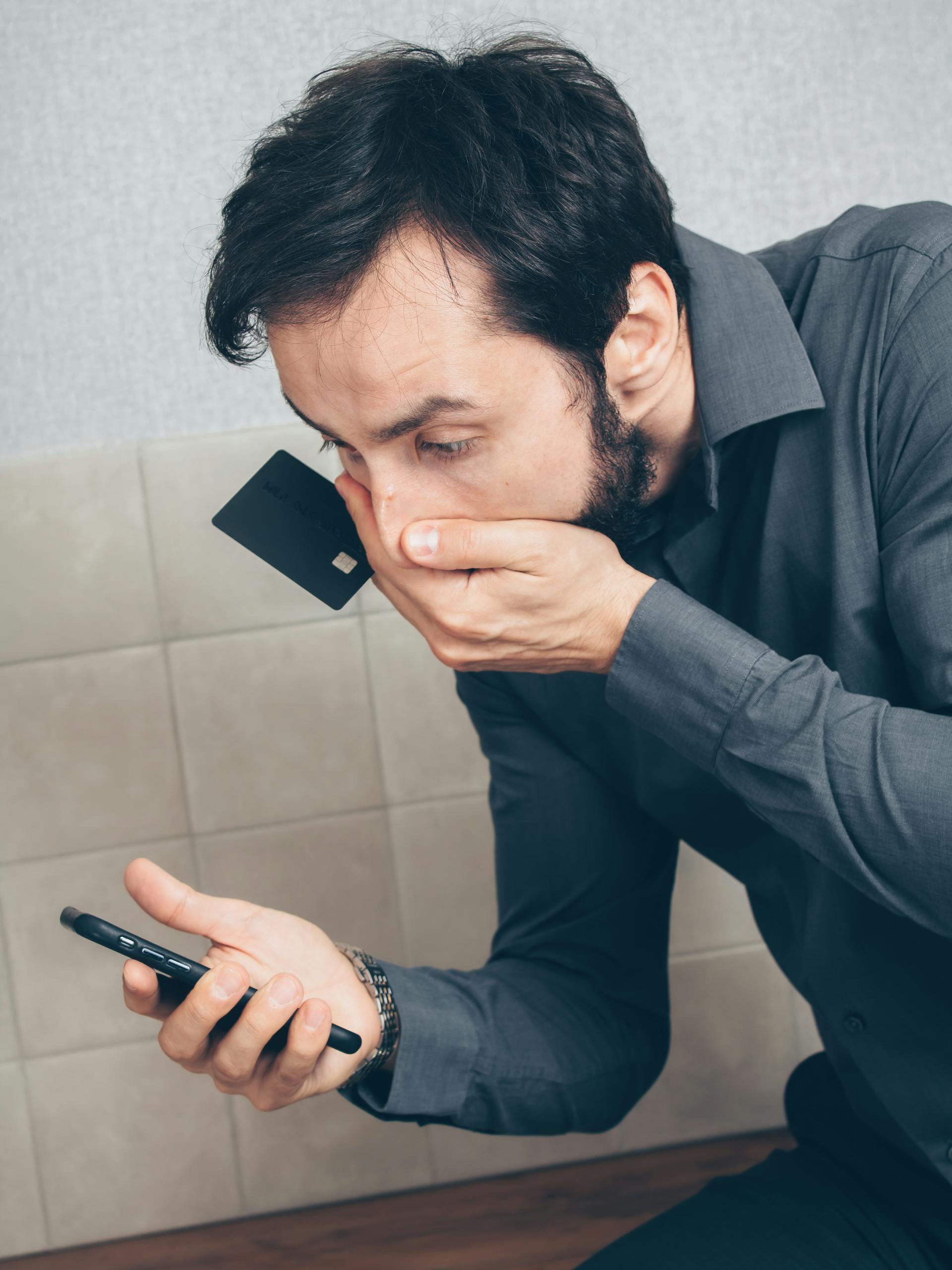Un hombre con una tarjeta de crédito en la mano mirando atónito su teléfono | Fuente: Pexels