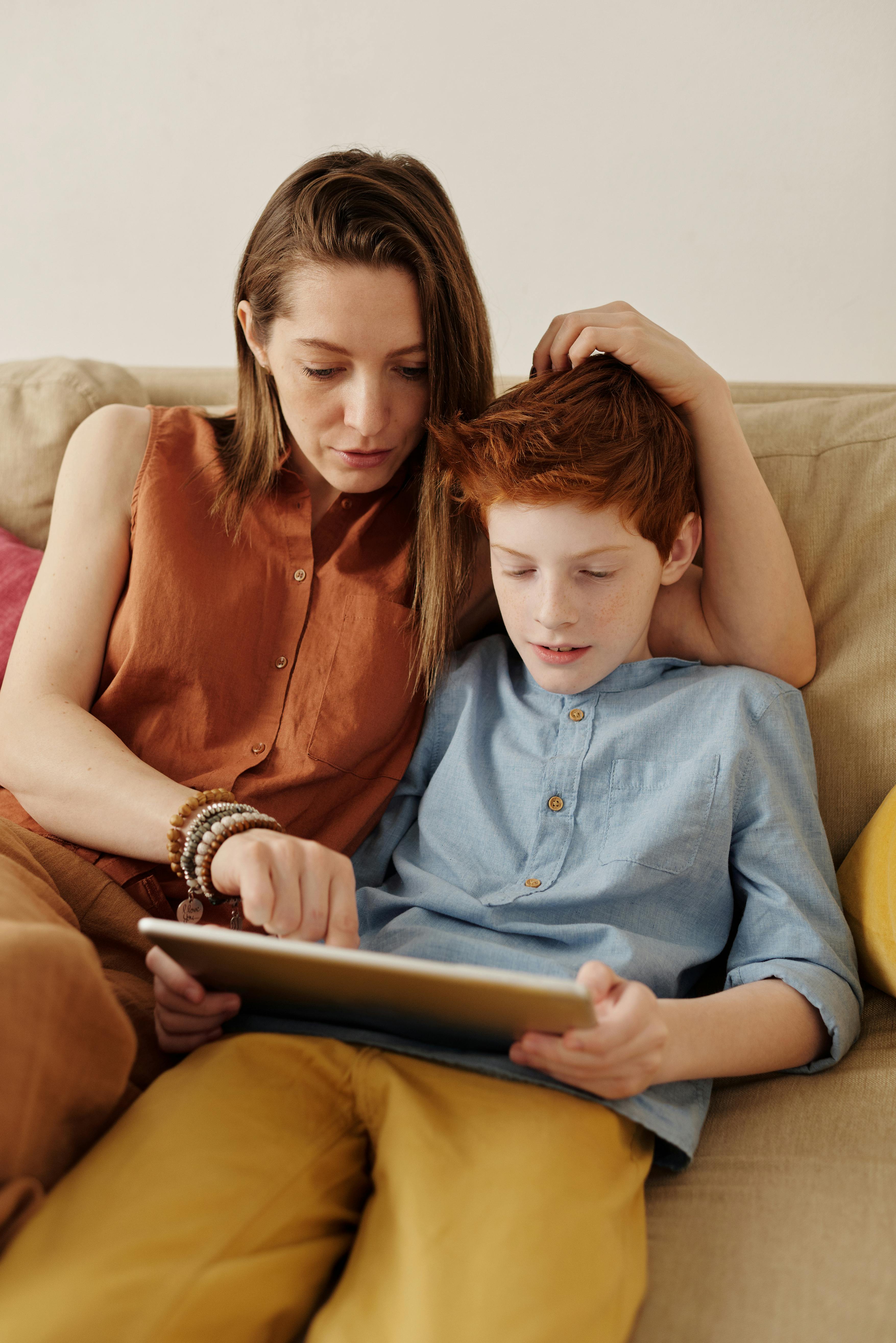 Una madre y su hijo sentados en un sofá mirando una tablet | Fuente:  Pexels