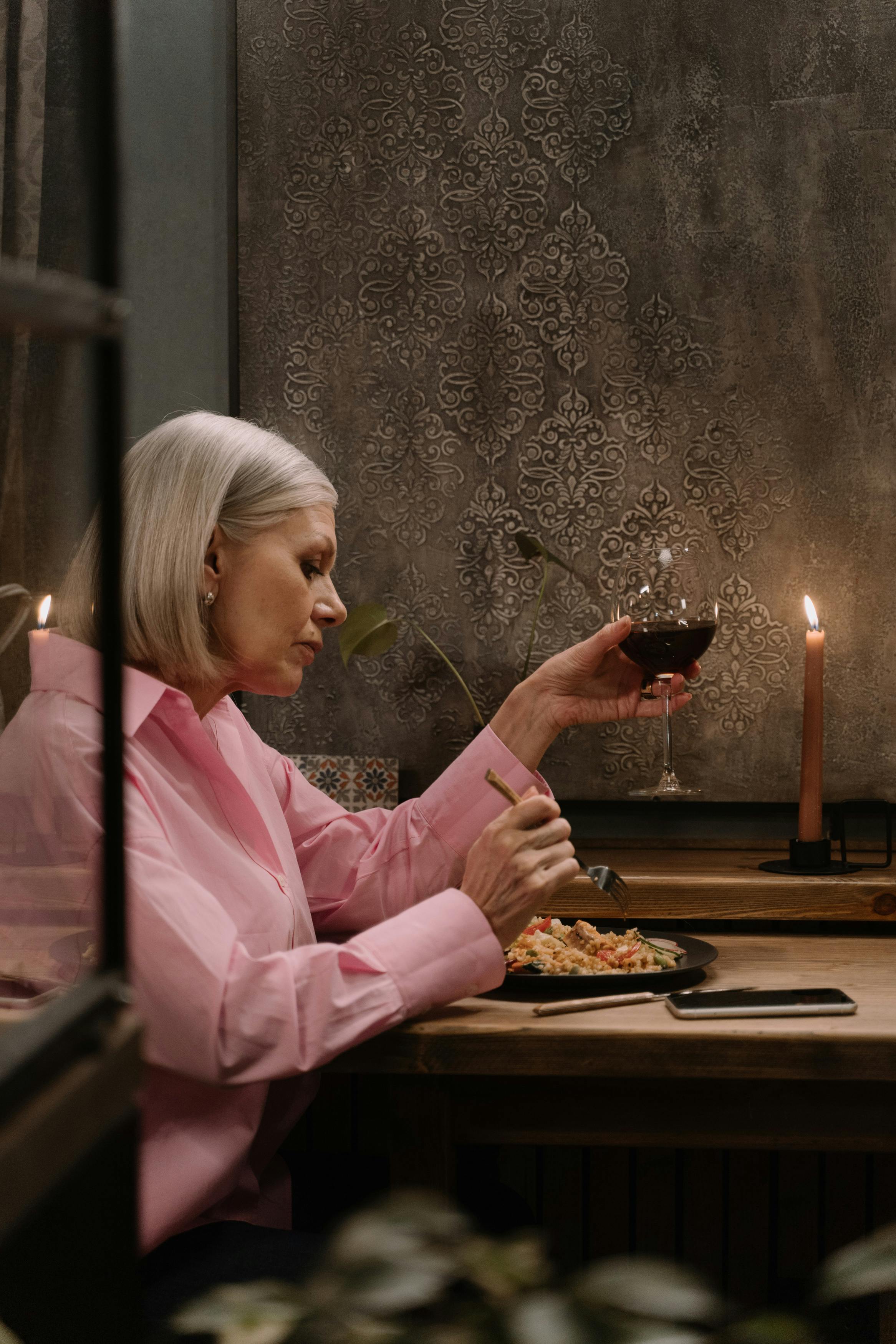 Mujer sosteniendo una copa de vino mientras come | Fuente: Pexels