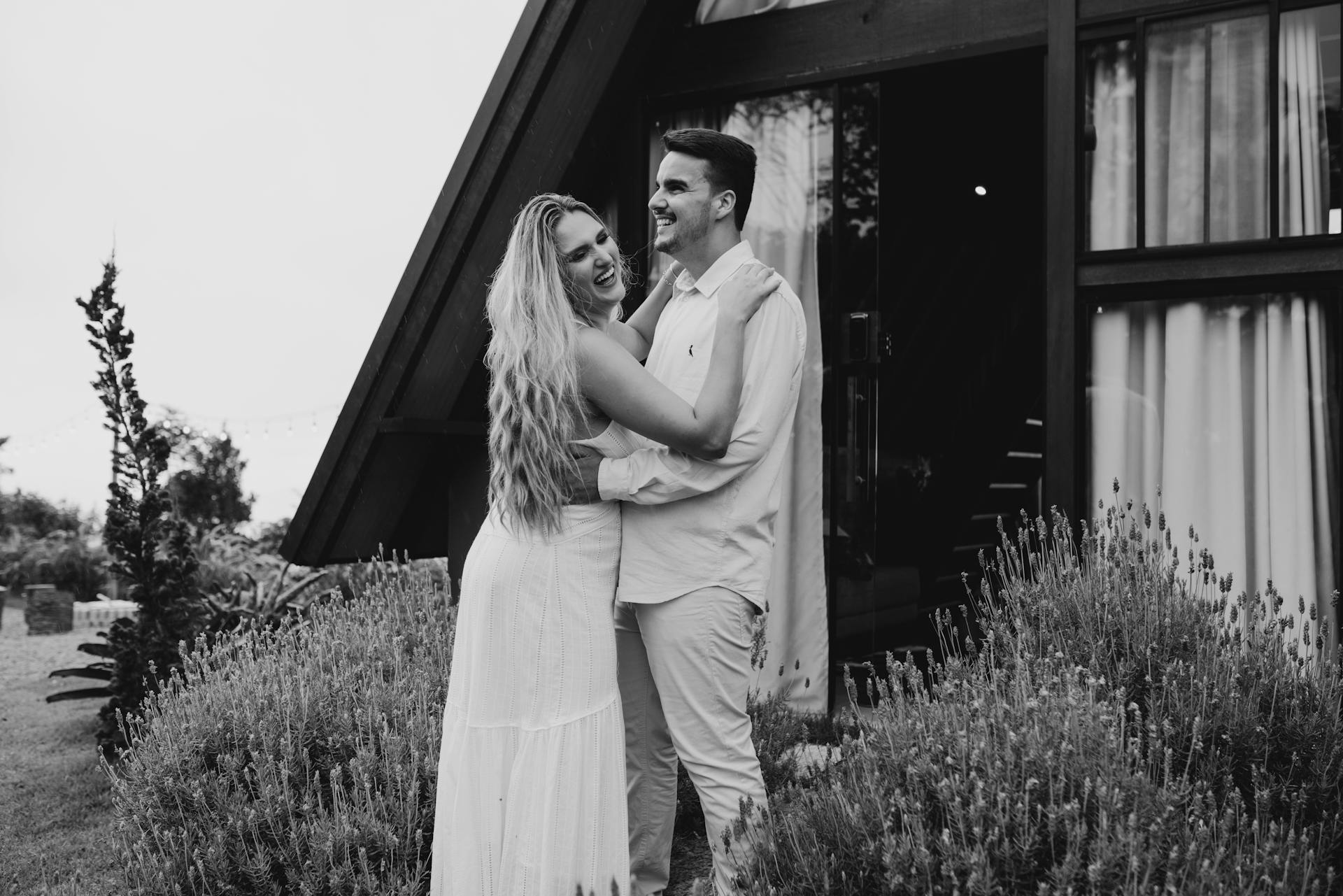 Una pareja sonriente se abraza frente a una moderna cabaña | Fuente: Pexels