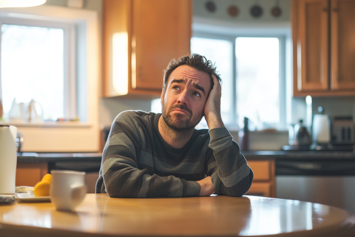 Un hombre sentado a la mesa de la cocina | Fuente: Midjourney