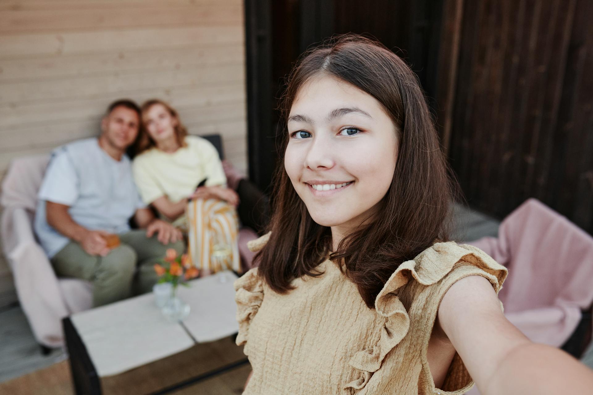 Una adolescente tomándose un selfie con dos adultos al fondo | Fuente: Pexels