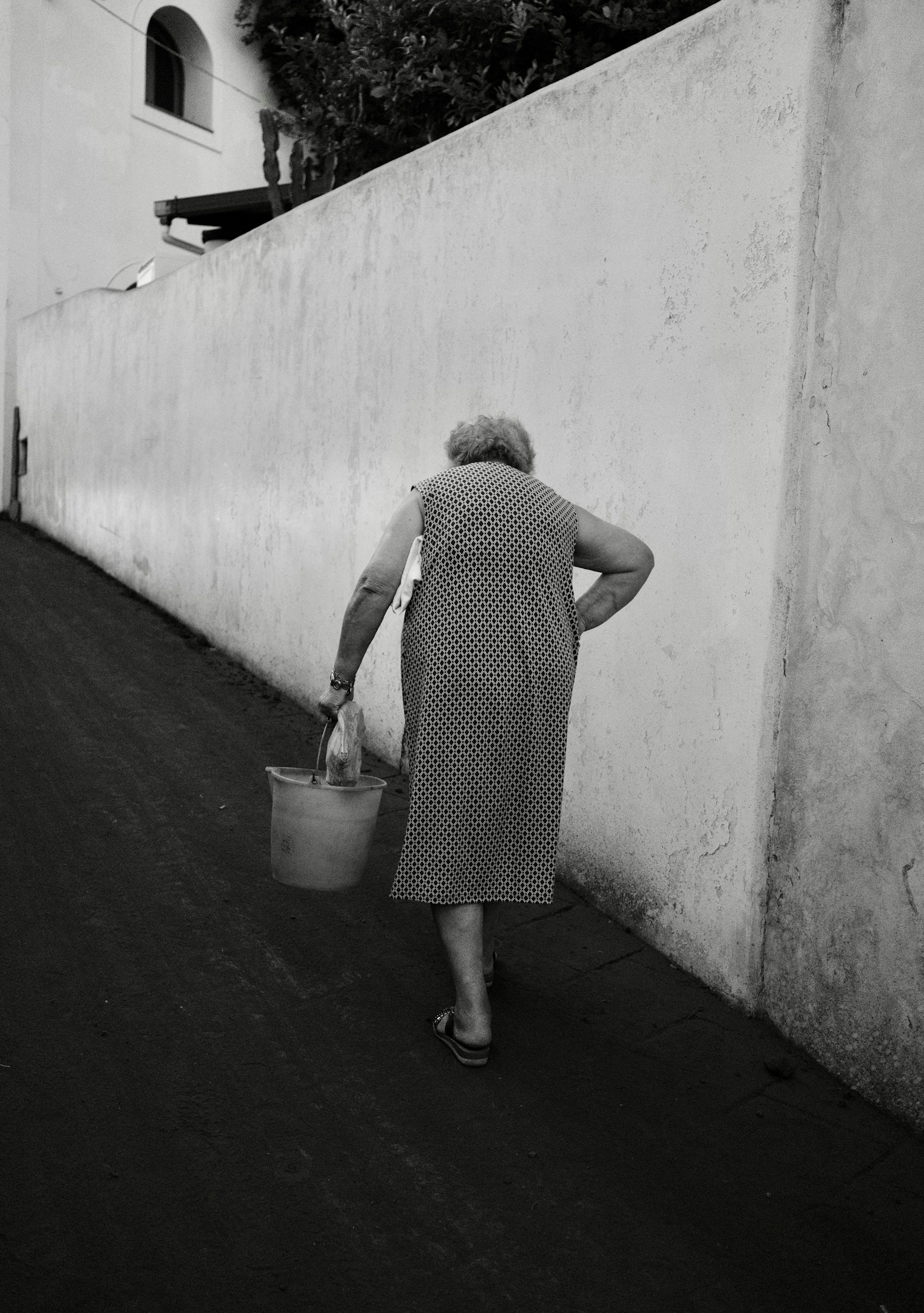 Toma en escala de grises de una mujer mayor caminando con un cubo | Fuente: Unsplash