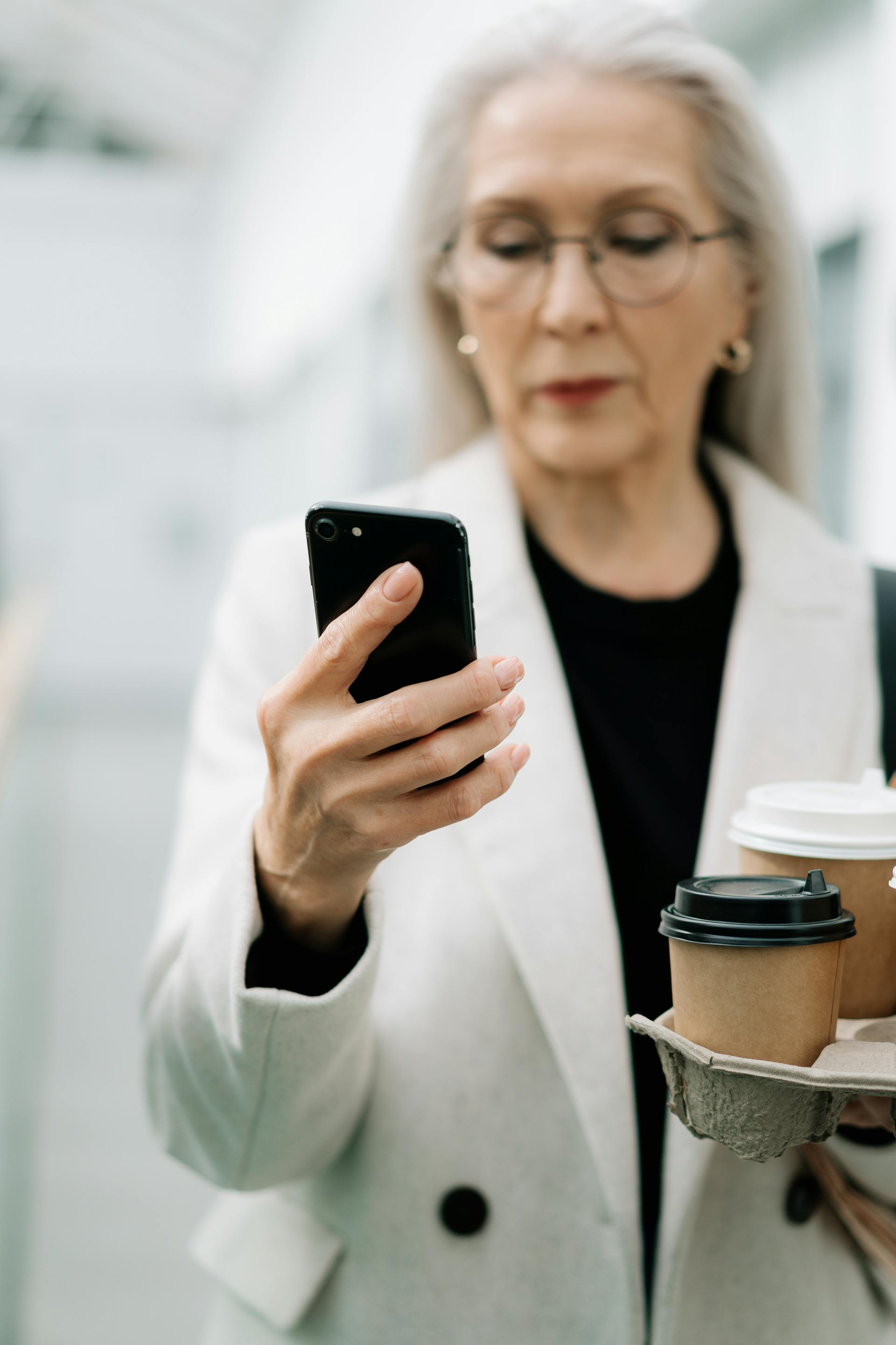 Una anciana usando su teléfono mientras sostiene un café | Fuente: Pexels