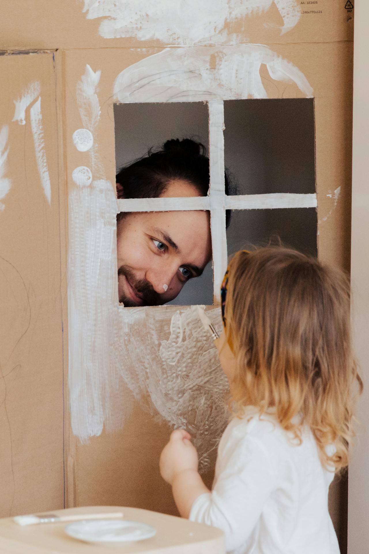 Un hombre jugando con su hija pequeña mientras pinta su casita de juguete | Fuente: Pexels