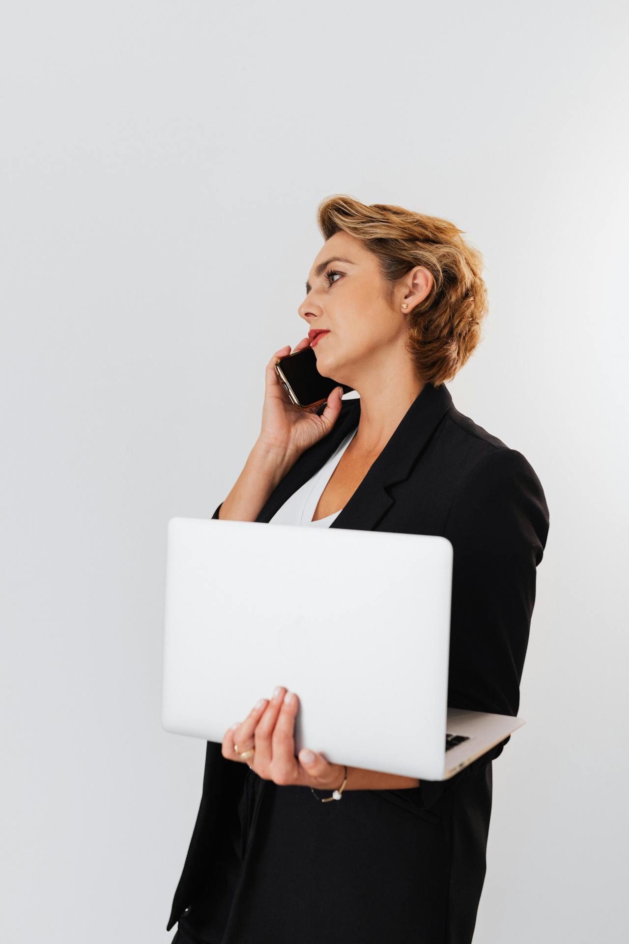 Una mujer atendiendo una llamada telefónica mientras sostiene una computadora portátil | Fuente: Pexels