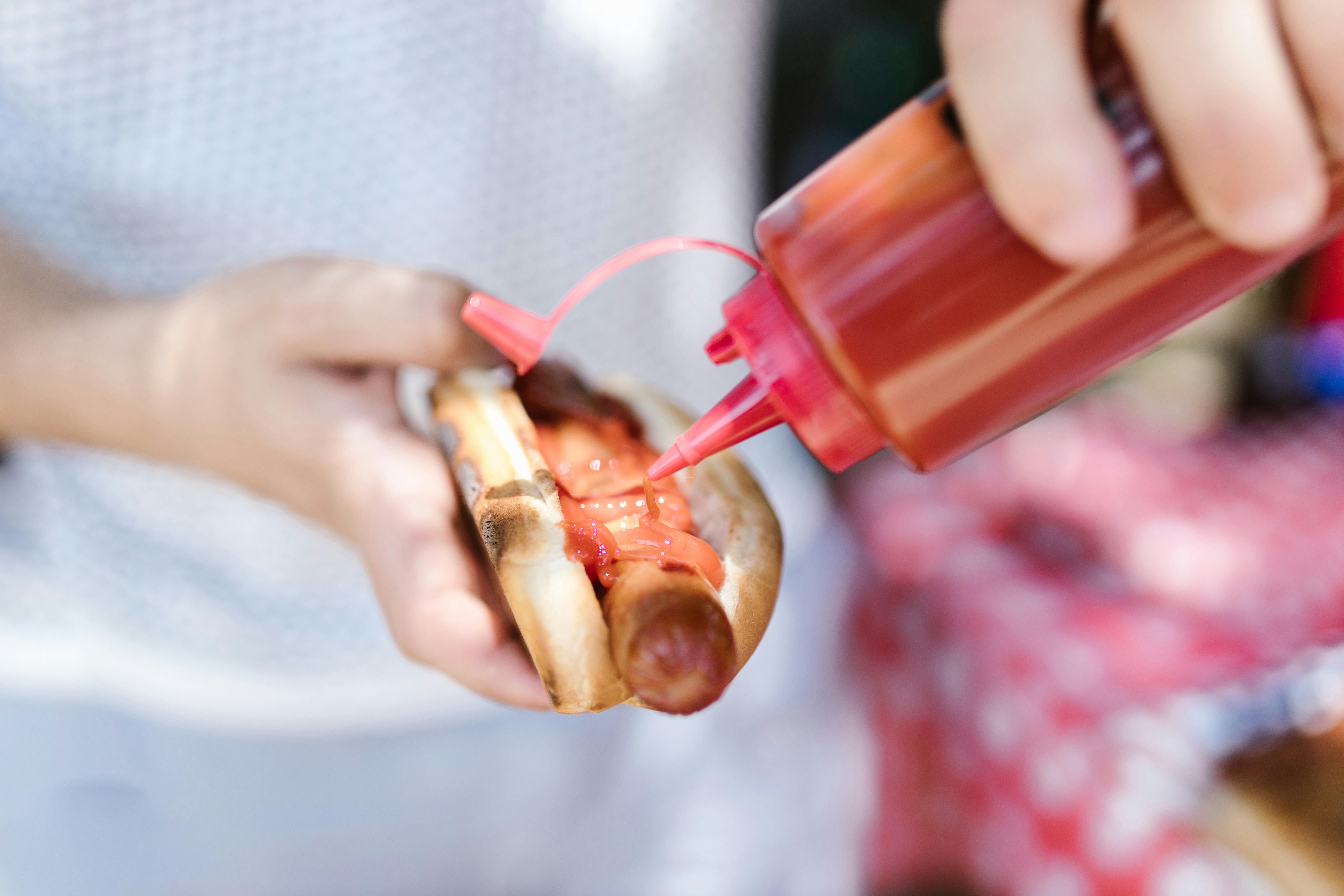 Una persona poniendo ketchup en un perrito caliente | Fuente: Pexels